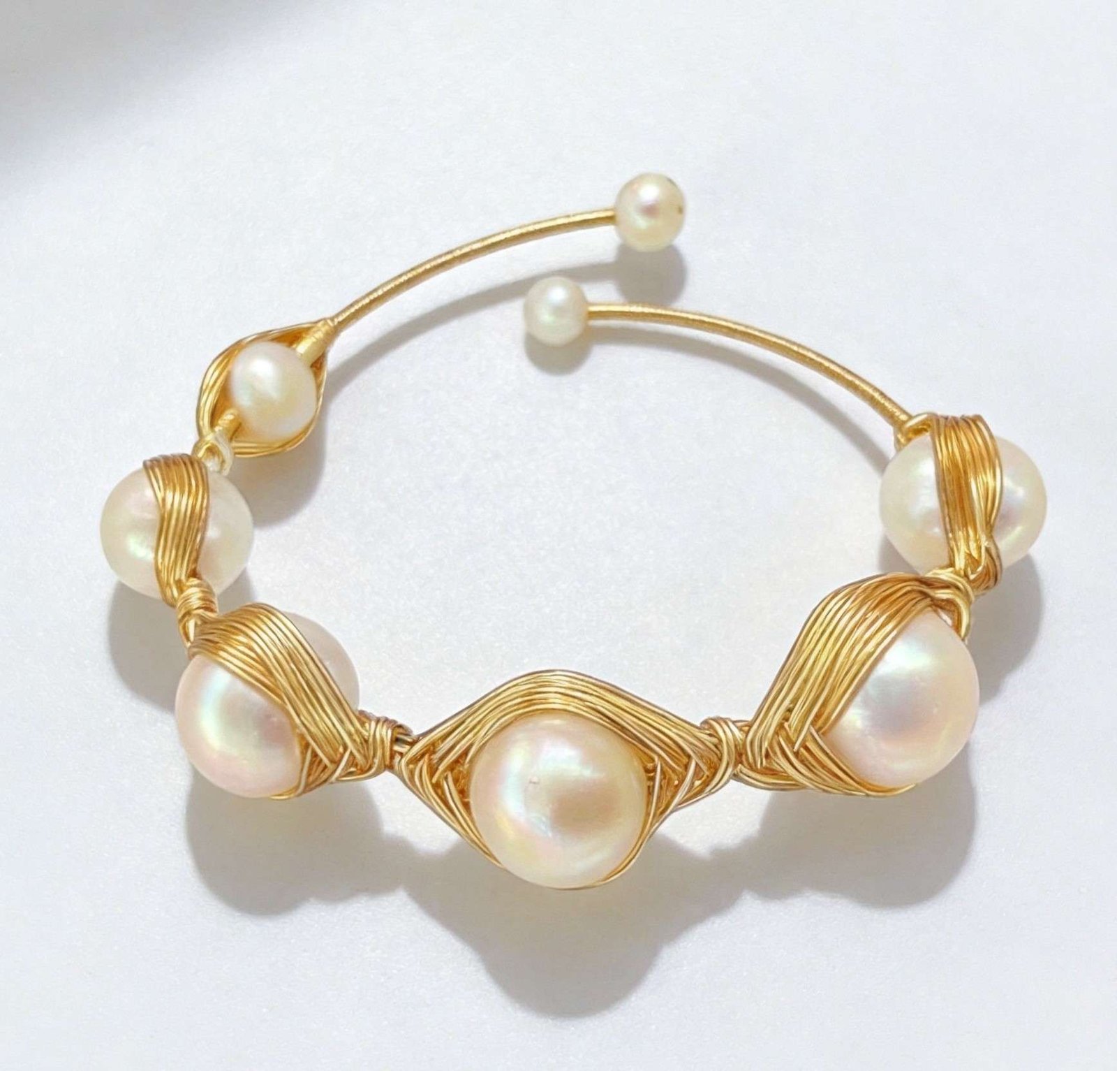 An elegant gold wire-wrapped bracelet with large round pearls, minimalist design on white background
